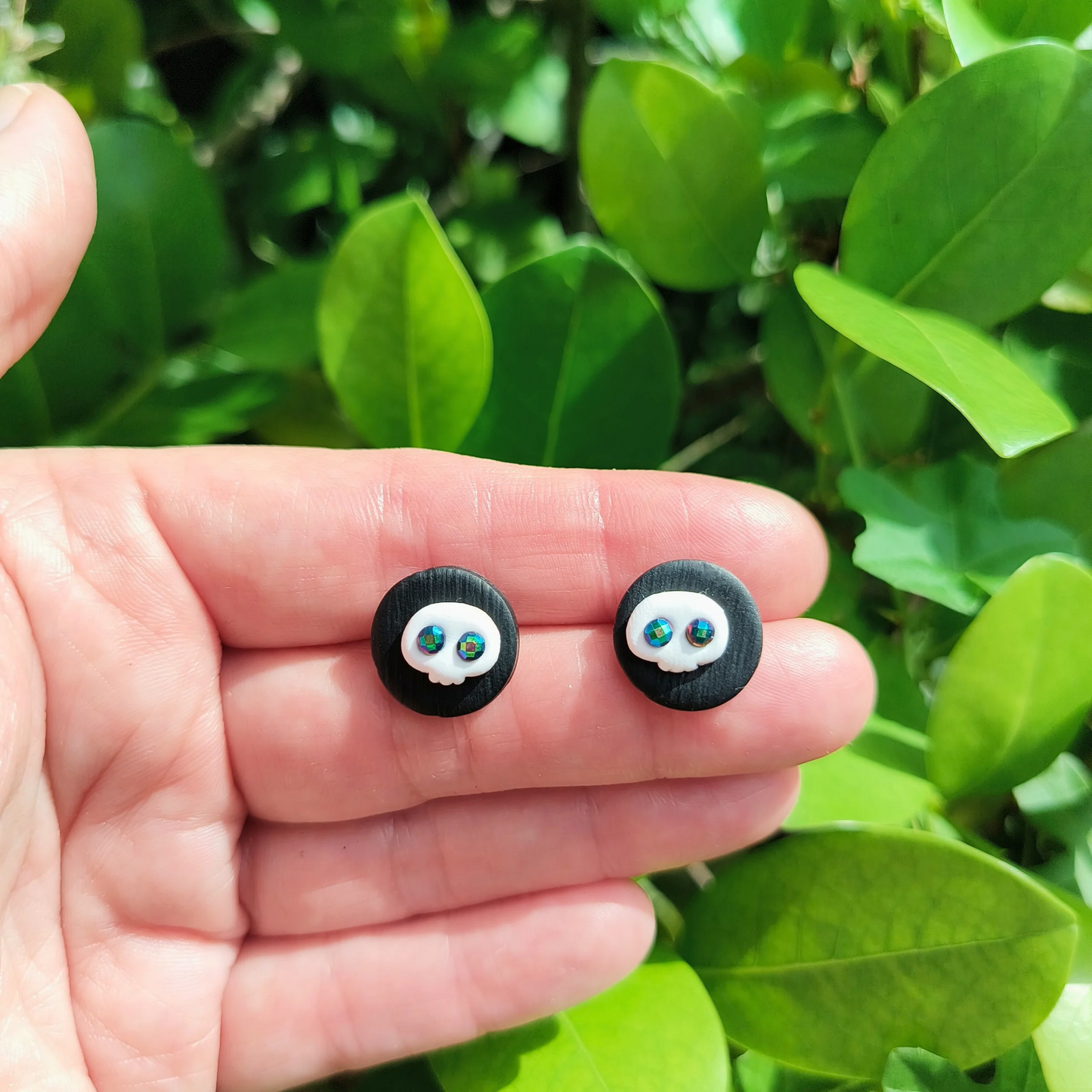 A hand holding a black and white pair of skull stud earrings.