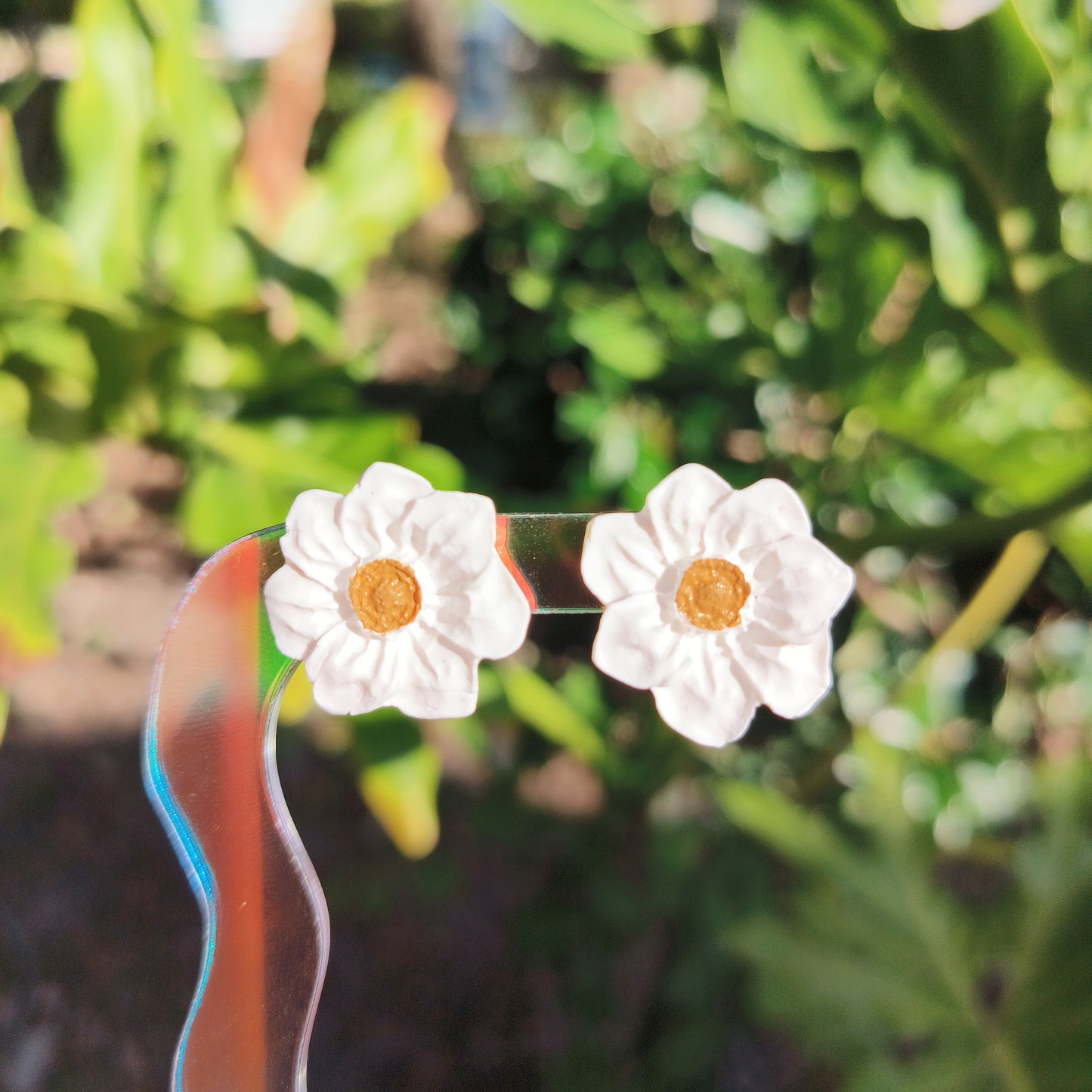 White flower earrings held against a green leafy background