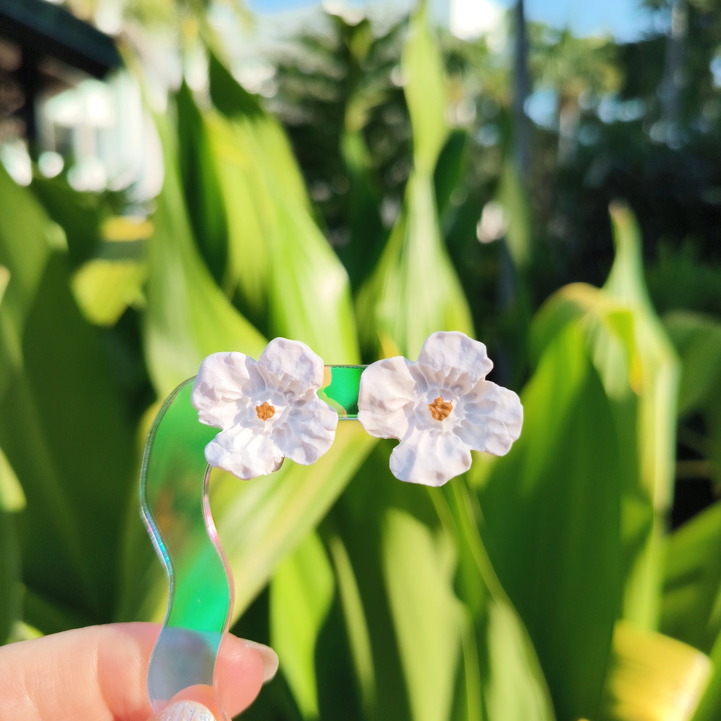 Floral earrings held against a green leafy background