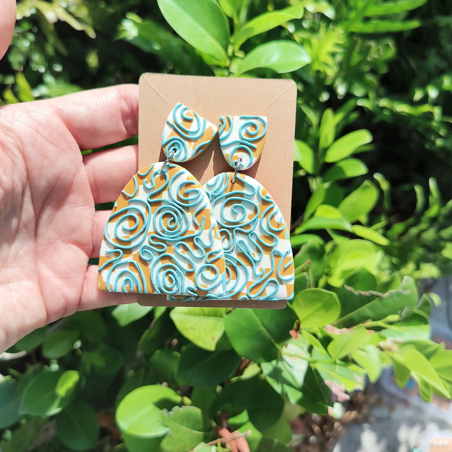 Large, dangle earrings that are white and mustard checkerboard , with a swirly blue design on top