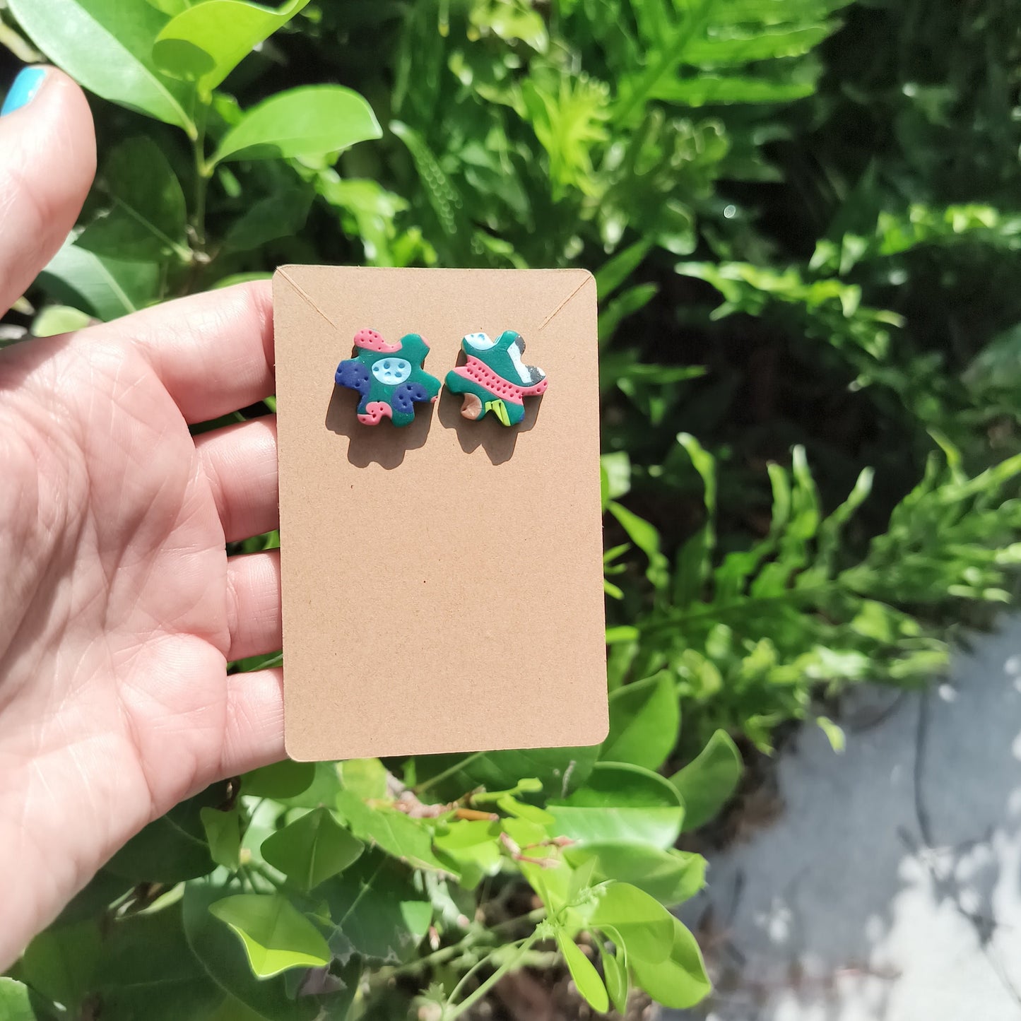 Multicolored, textured polymer clay studs in a flower shape, against a backdrop of green foliage.