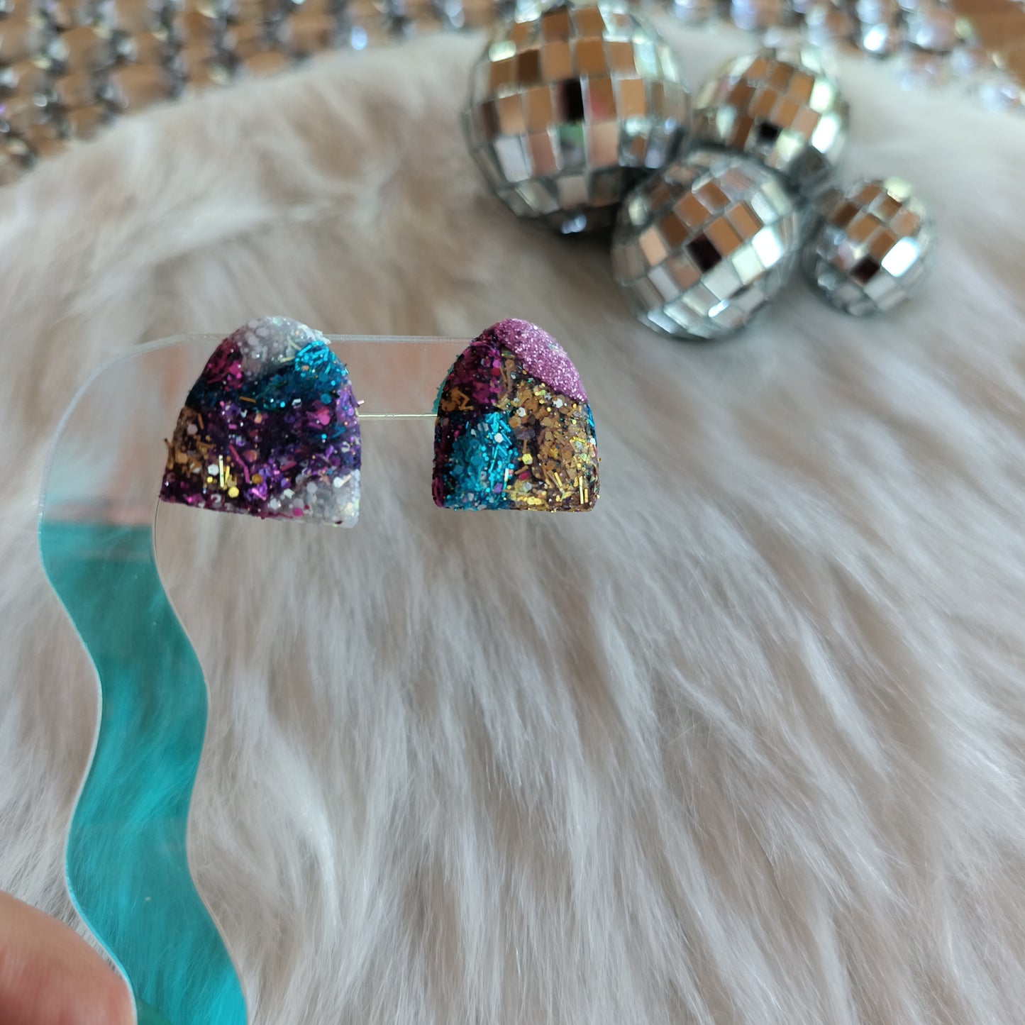 Colorful glittery earrings on a white fur background.