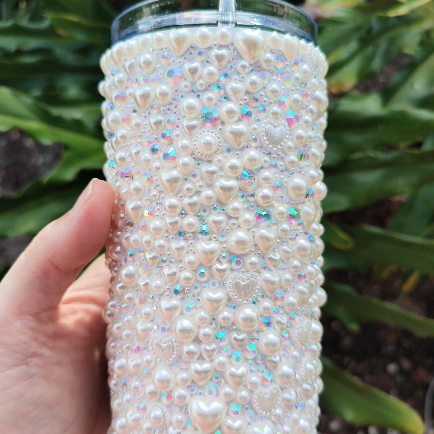 photo of the details of this white stainless-steel tumbler that is bedazzled with pearl hearts of varying sizes, ab rhinestones of varying sizes, and pearls of varying sizes. bpa free plastic lid featured.