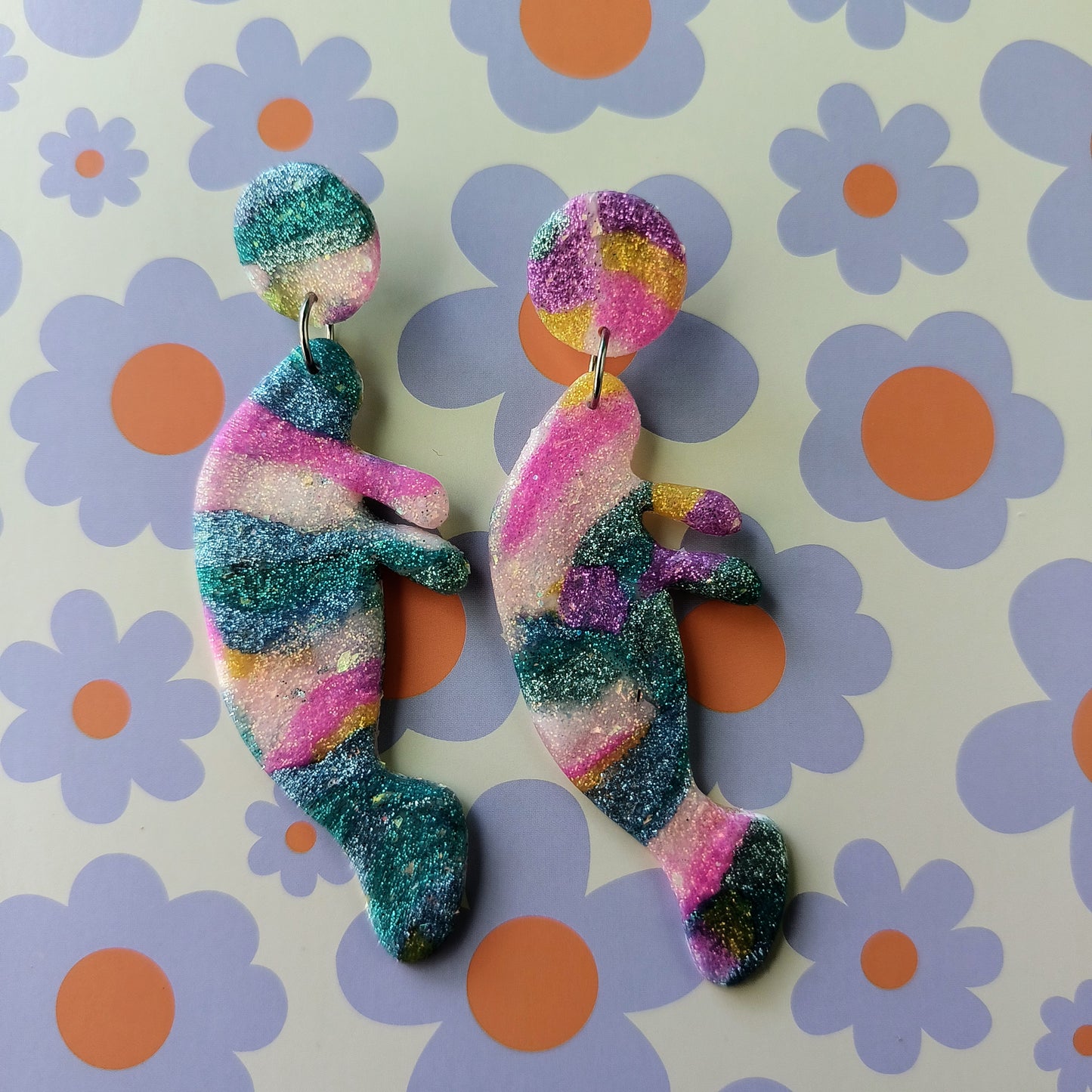 Colorful manatee glittery earrings on a floral background