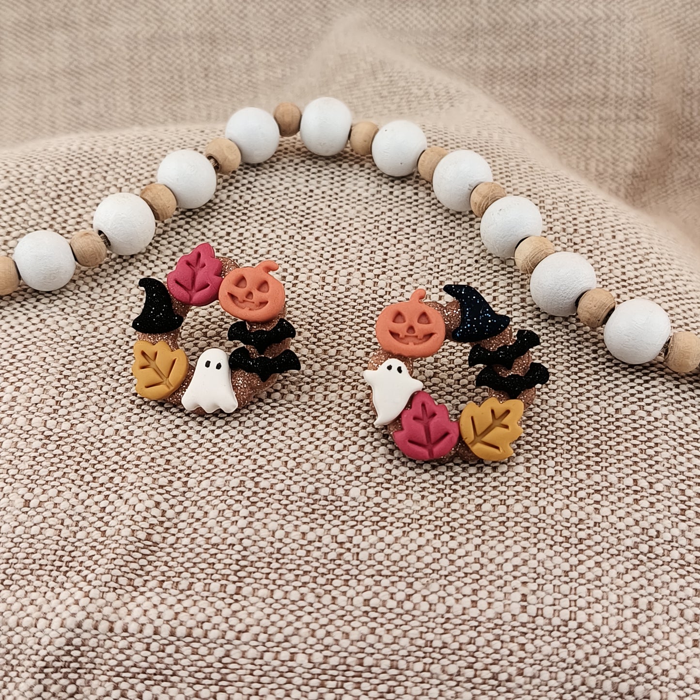 Halloween-themed wreath earrings on a textured beige surface