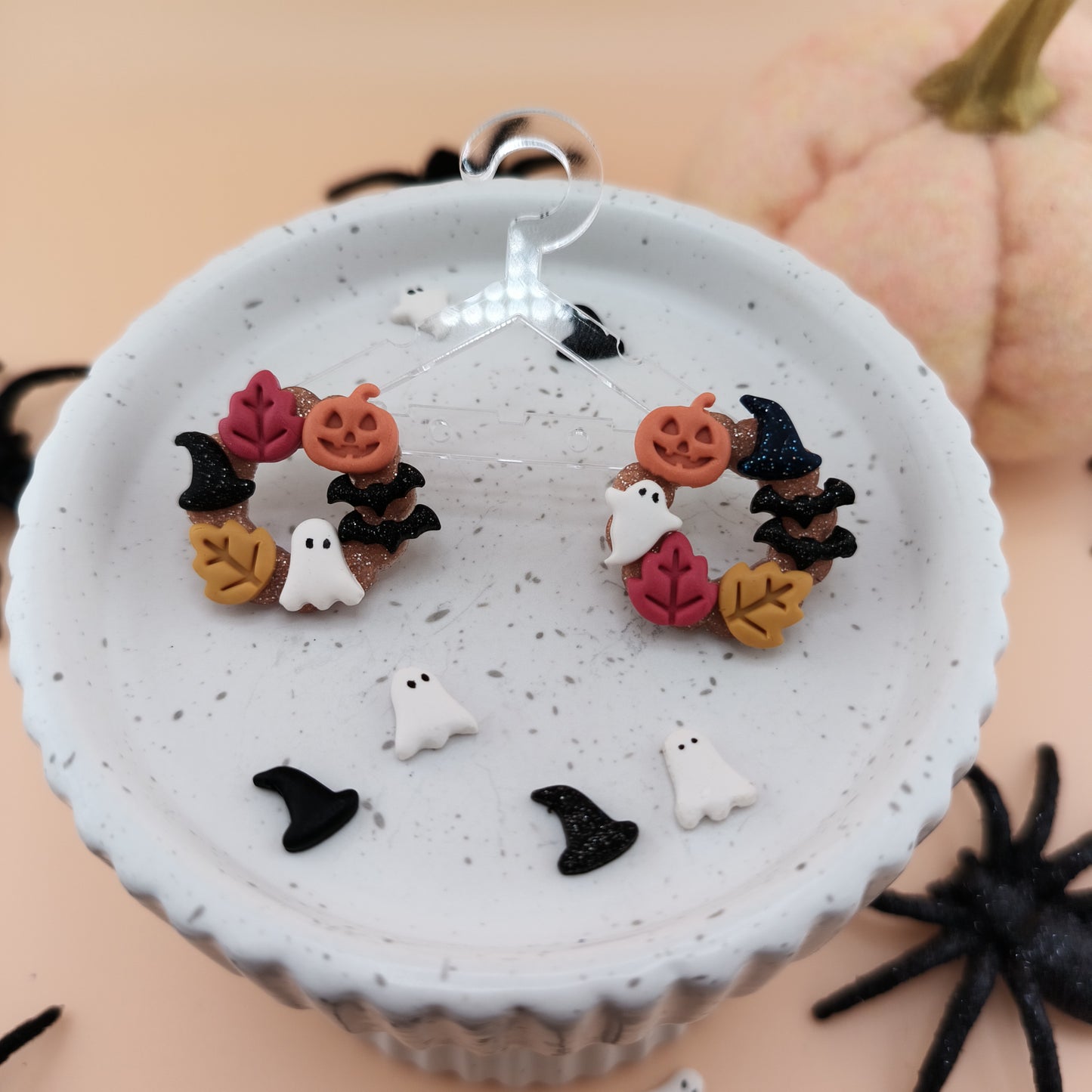 Halloween-themed earrings on a white dish with pumpkins and spider in the background