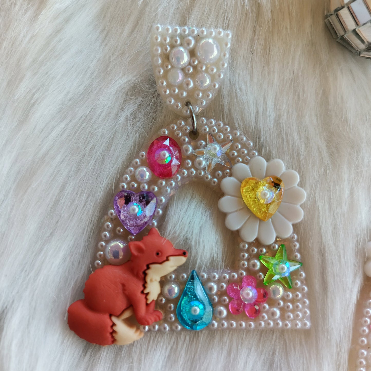 Bedazzled earrings with fox and colorful beads on fur background