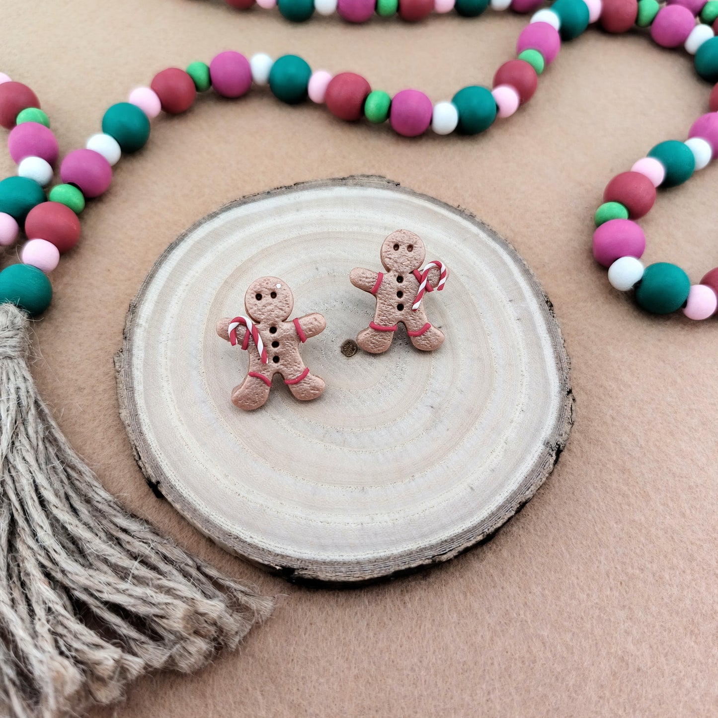 Two gingerbread man earrings on a wooden disc with a colorful bead garland in the background.