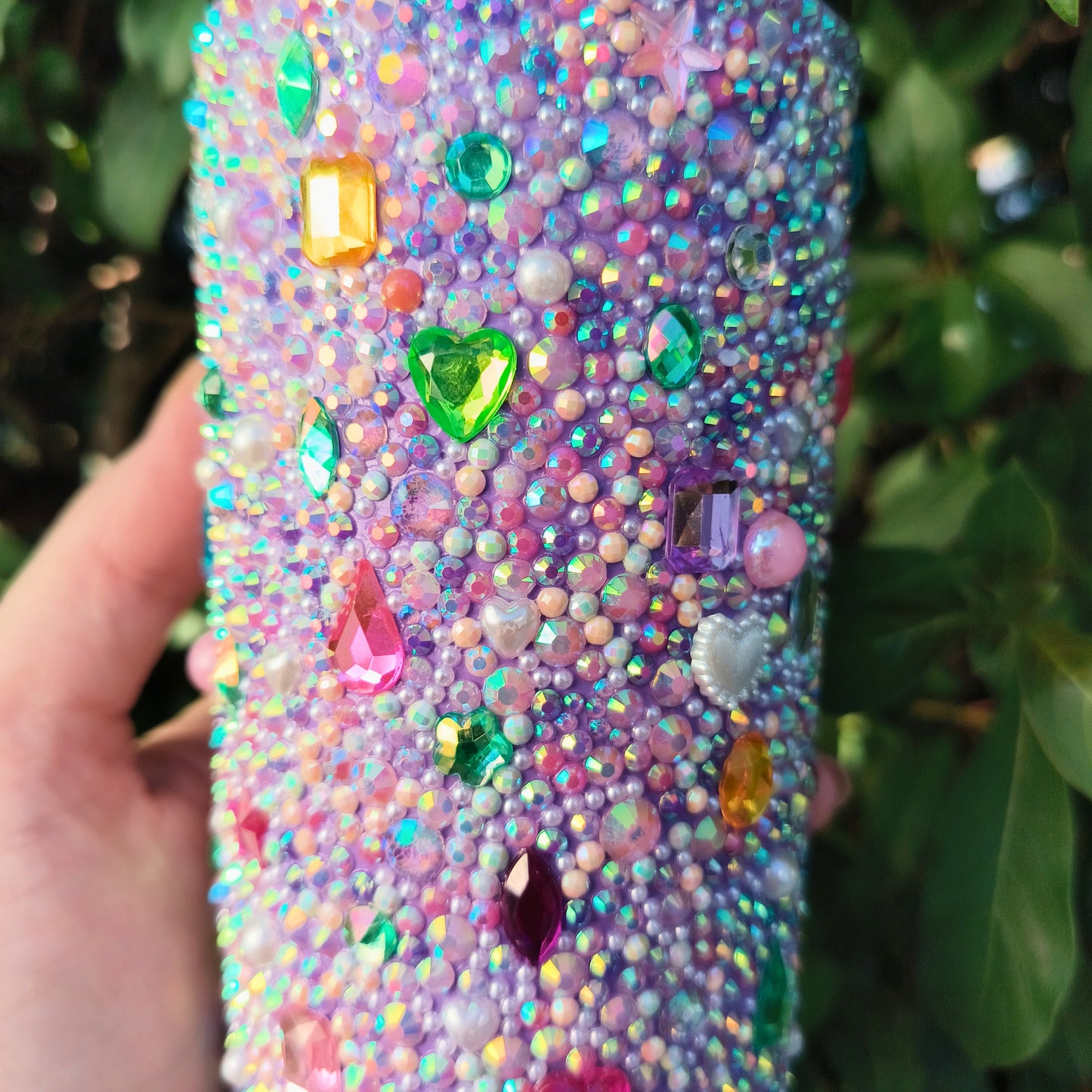 Drink tumbler with colorful gemstones held by a hand against a green leafy background