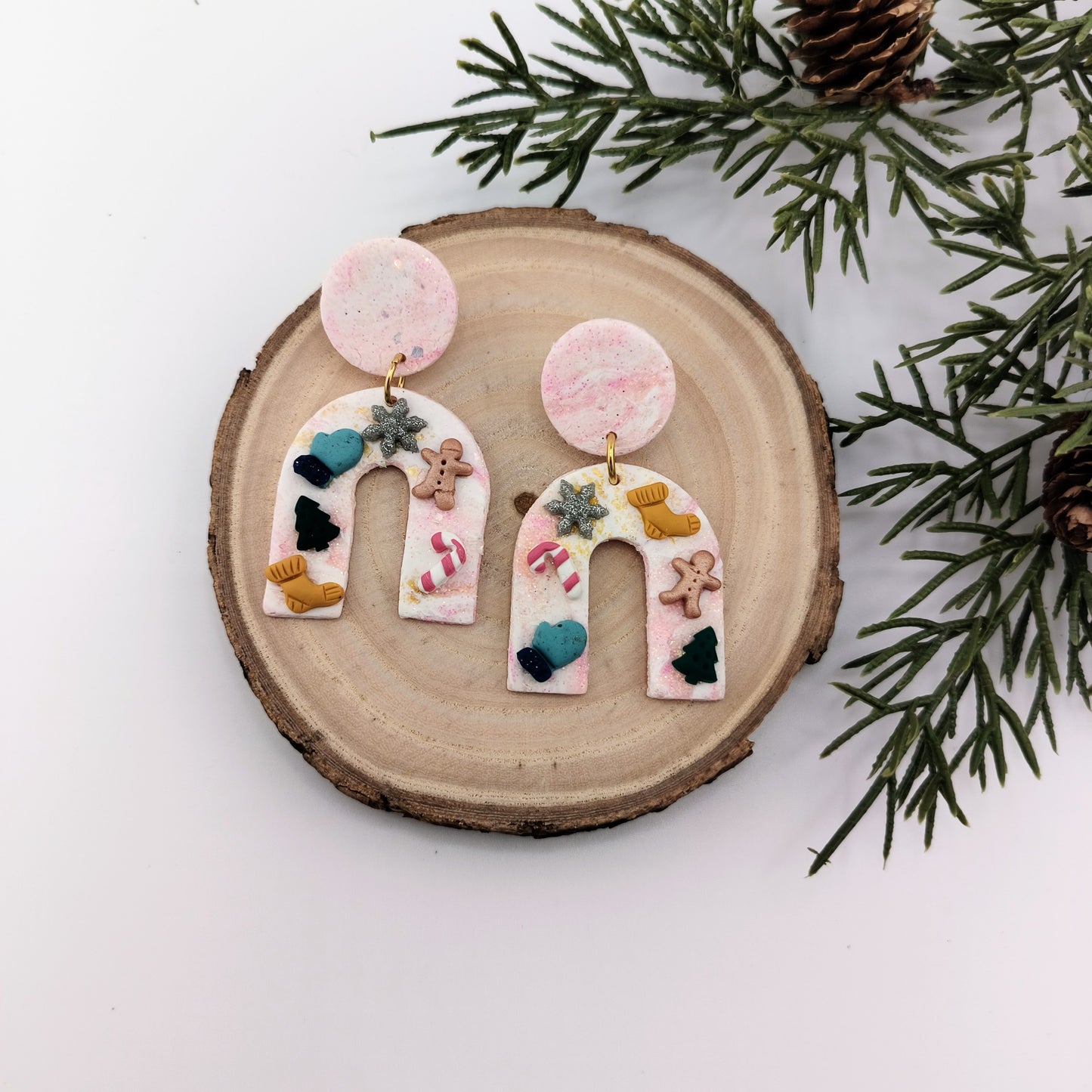 Decorative earrings with colorful Christmas details on a wooden surface with greenery.
