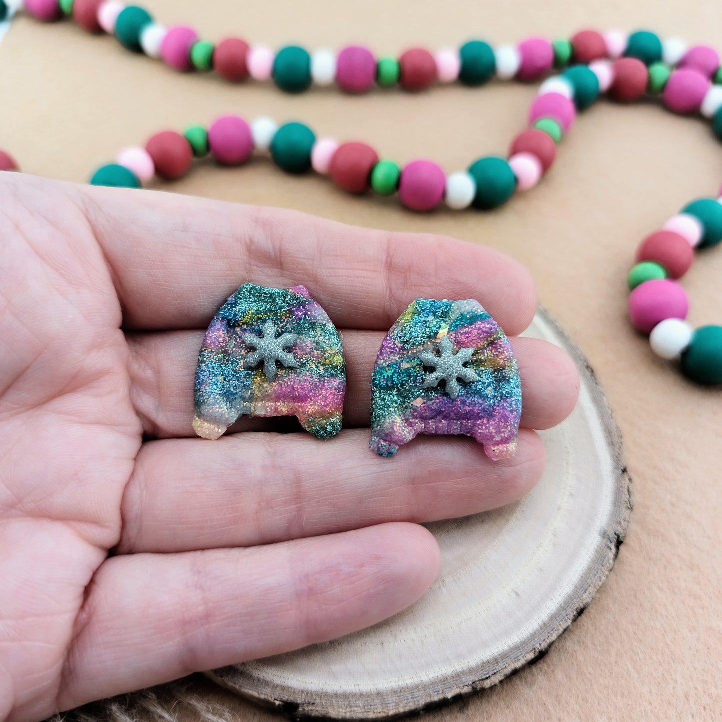 Colorful glittery sweater earrings held in a hand with a beaded garland in the background.