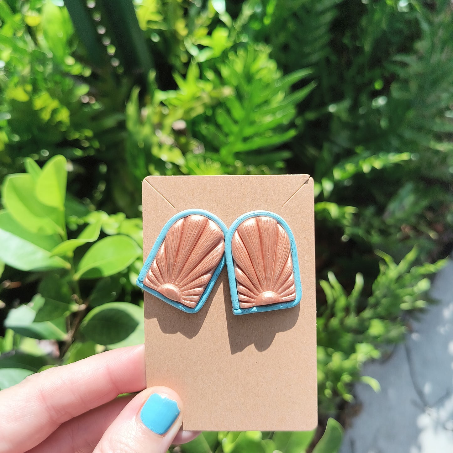 Rose Gold Polymer Clay Earrings with a Sunrise displayed on the front, against green foliage.