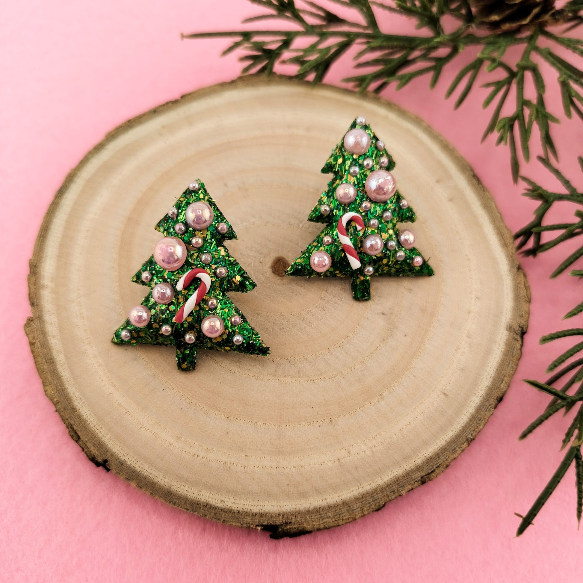 Christmas tree-shaped earrings with candy cane details on a wooden disc with a pink background