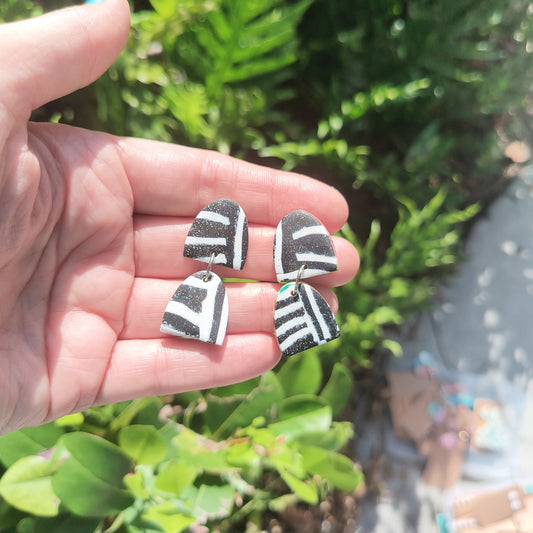 Black and white organic patterned dangle polymer clay earrings against the backdrop of green foliage.