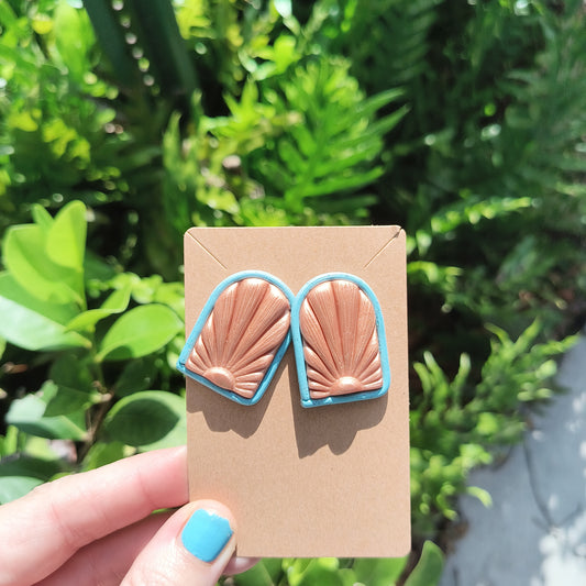 Rose Gold Polymer Clay Earrings with a Sunrise displayed on the front, against green foliage. 