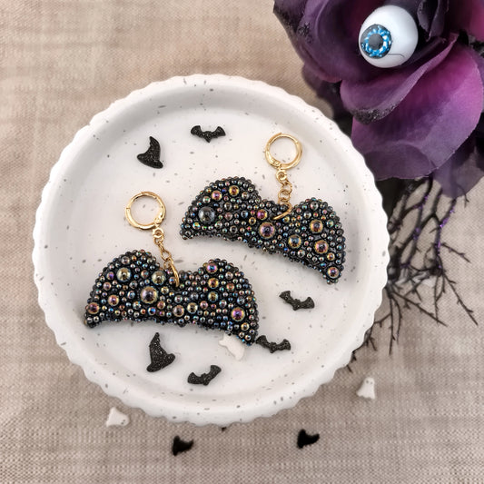 Black and gold bat earrings on a white dish with decorative elements on a beige background