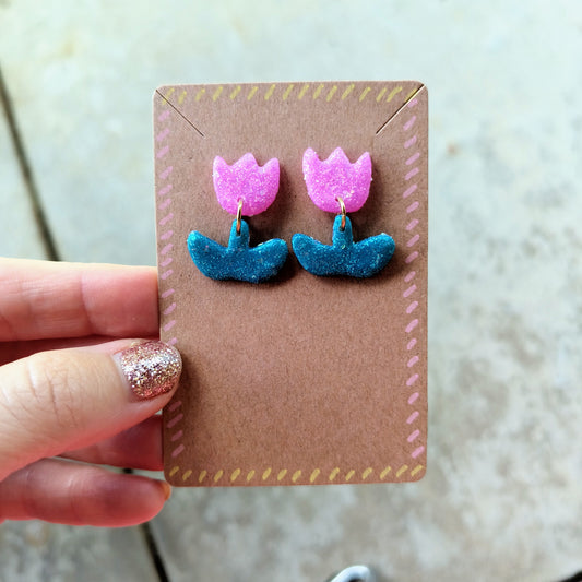 Pair of pink and green flower earrings on a brown card held by a hand.