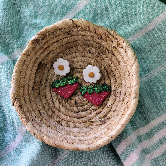 Woven dish with strawberry and flower earrings on a light blue fabric background