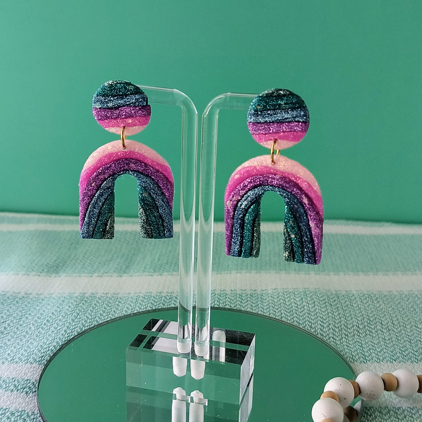 Colorful sparkle arch-shaped earrings on a clear stand against a green background