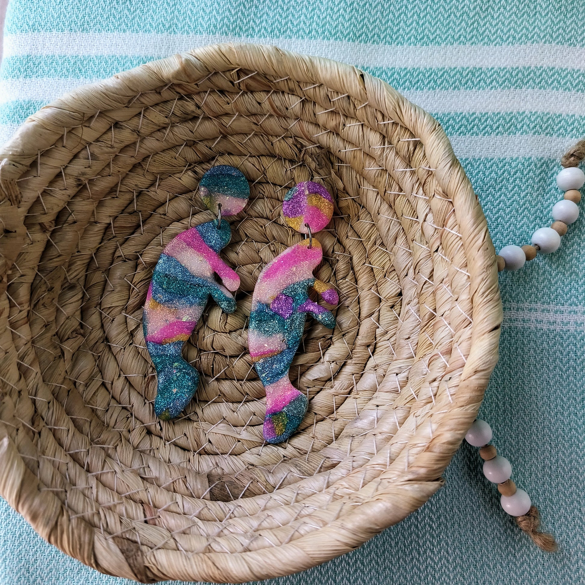 Colorful manatee earrings on a woven plate with a blue and white striped background