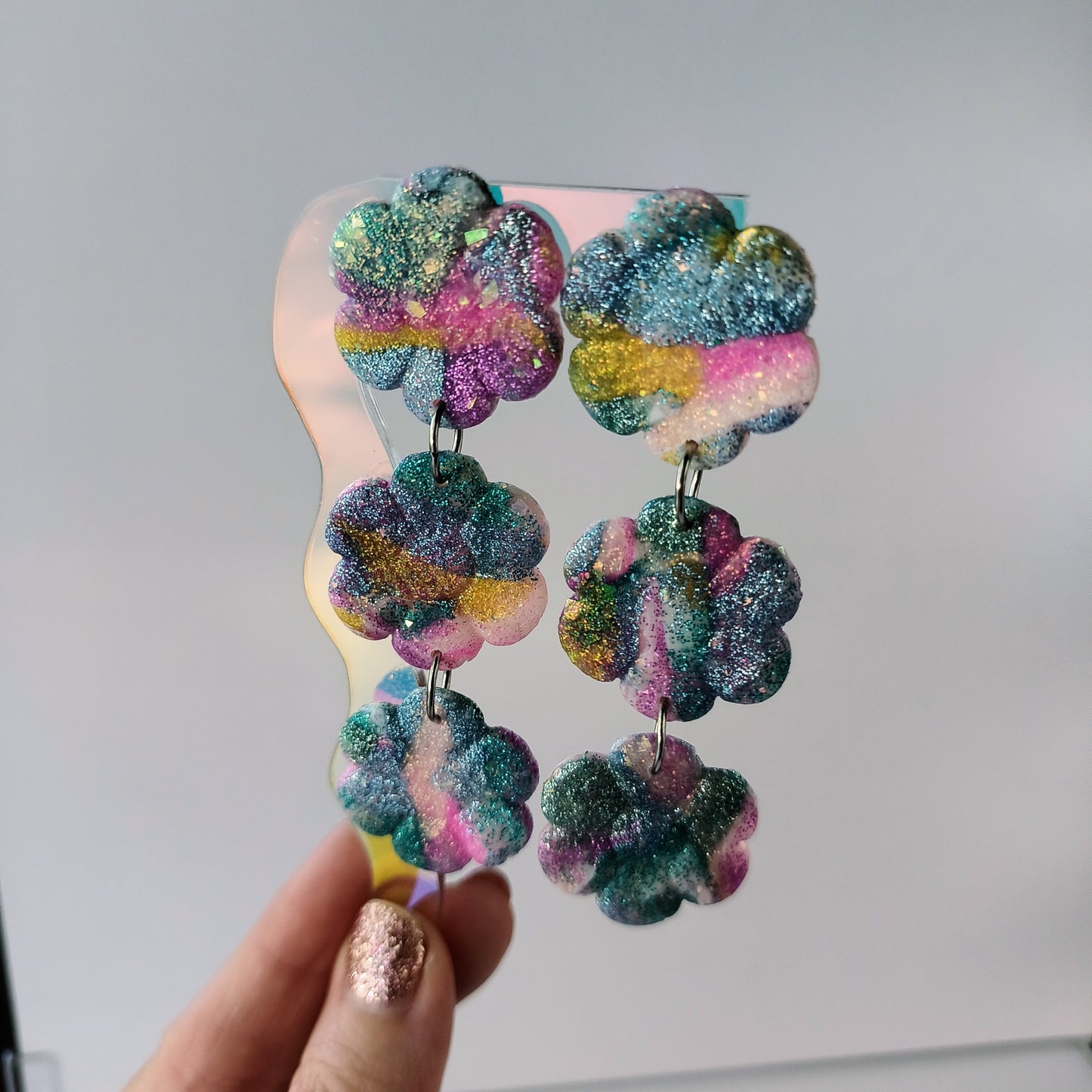 Colorful, sparkle flower-shaped earrings held by a hand against a neutral background