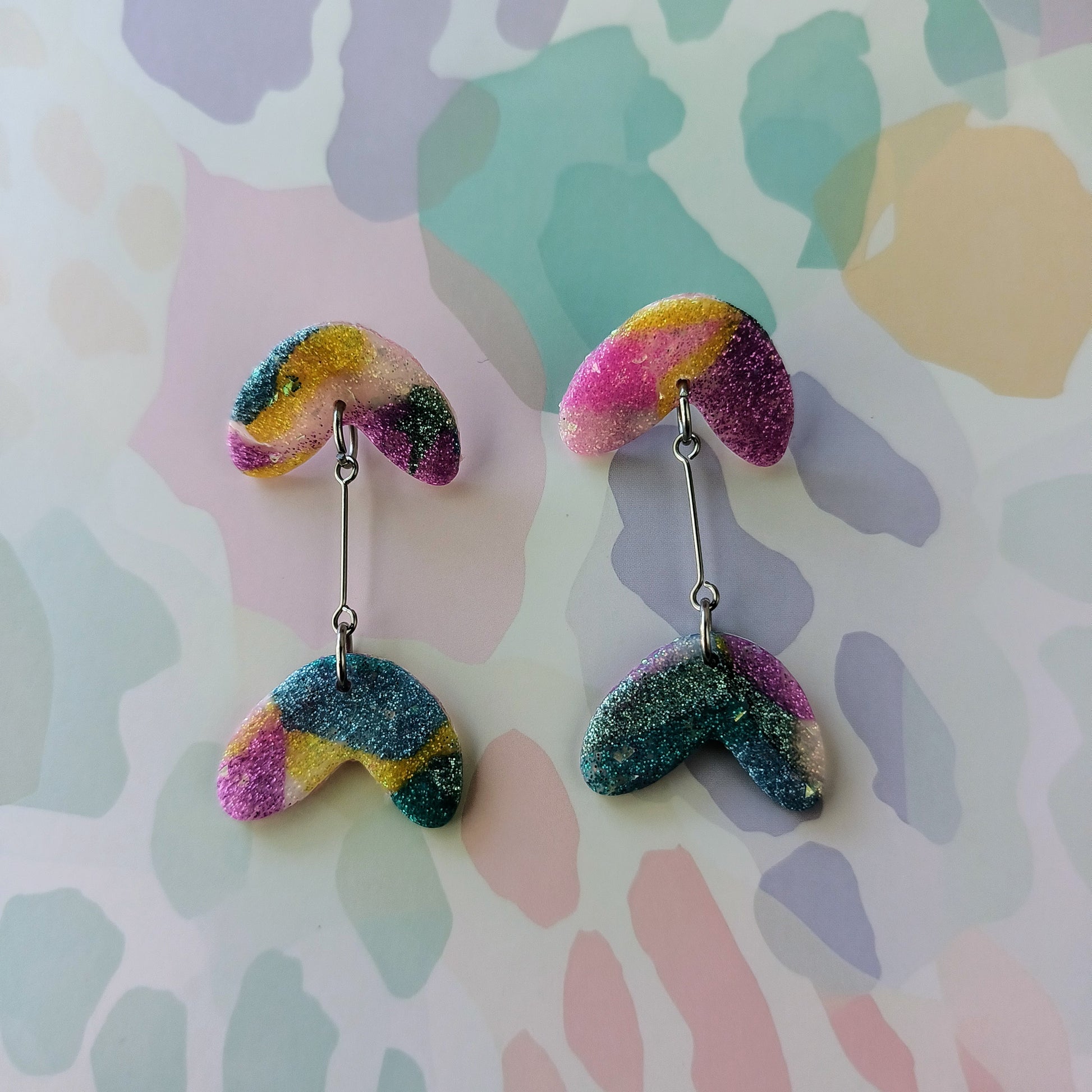 Colorful glittery earrings on a patterned background