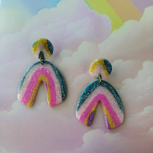Colorful sparkle earrings with rainbow design on a cloud-themed background