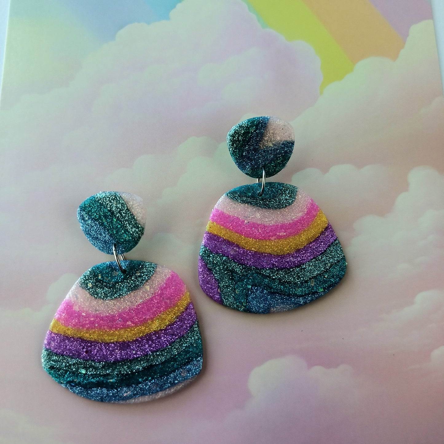 Rainbow layered polymer clay earrings on a pastel cloud background