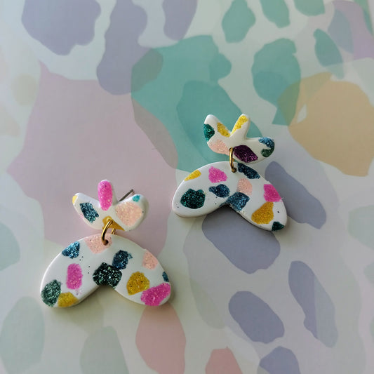 Butterfly-shaped earrings with colorful sparkle spots on a patterned background
