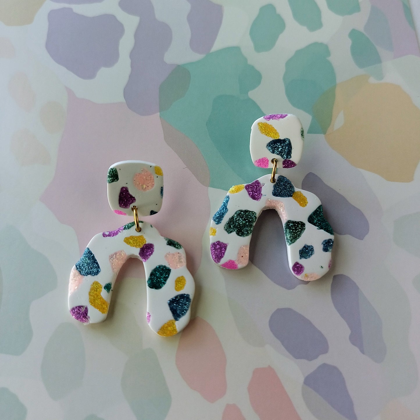 Colorful sparkle abstract earrings on a patterned background