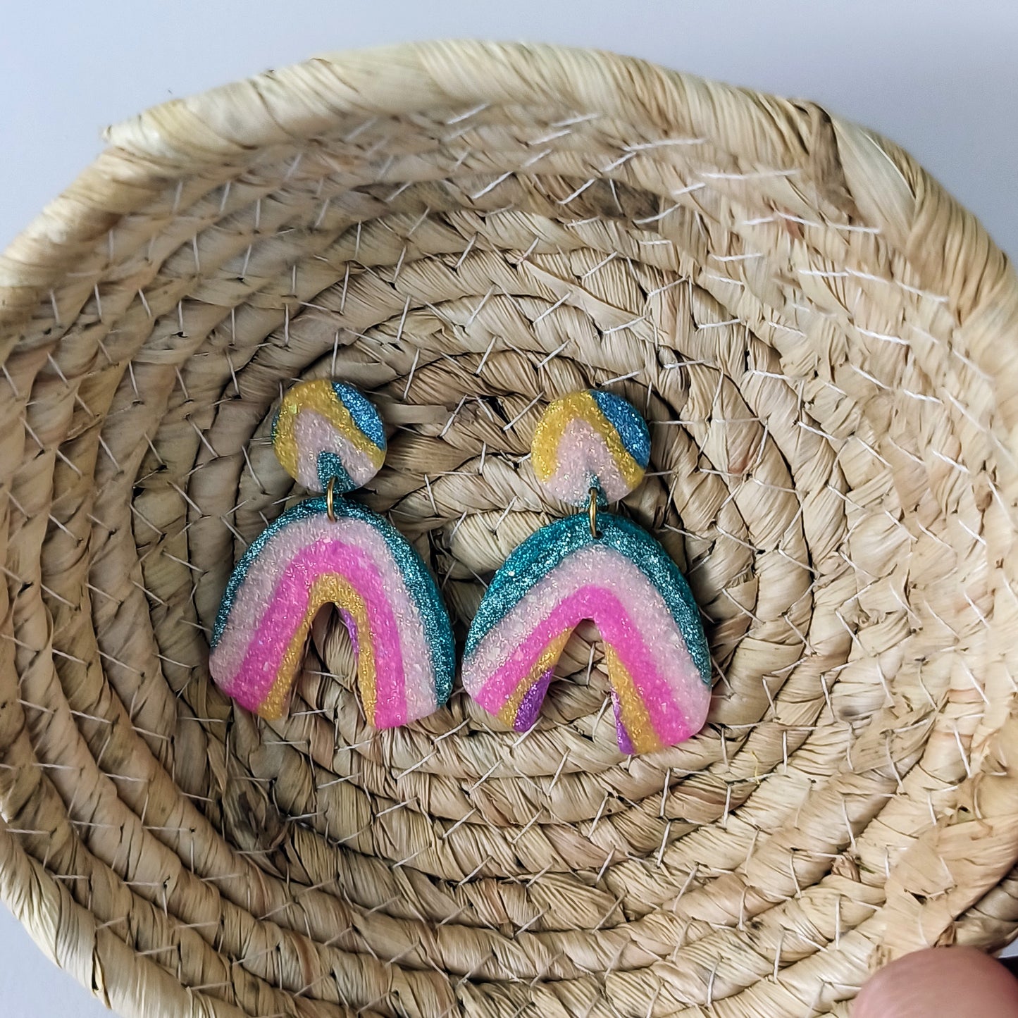 Colorful sparkle rainbow-shaped earrings on a woven basket