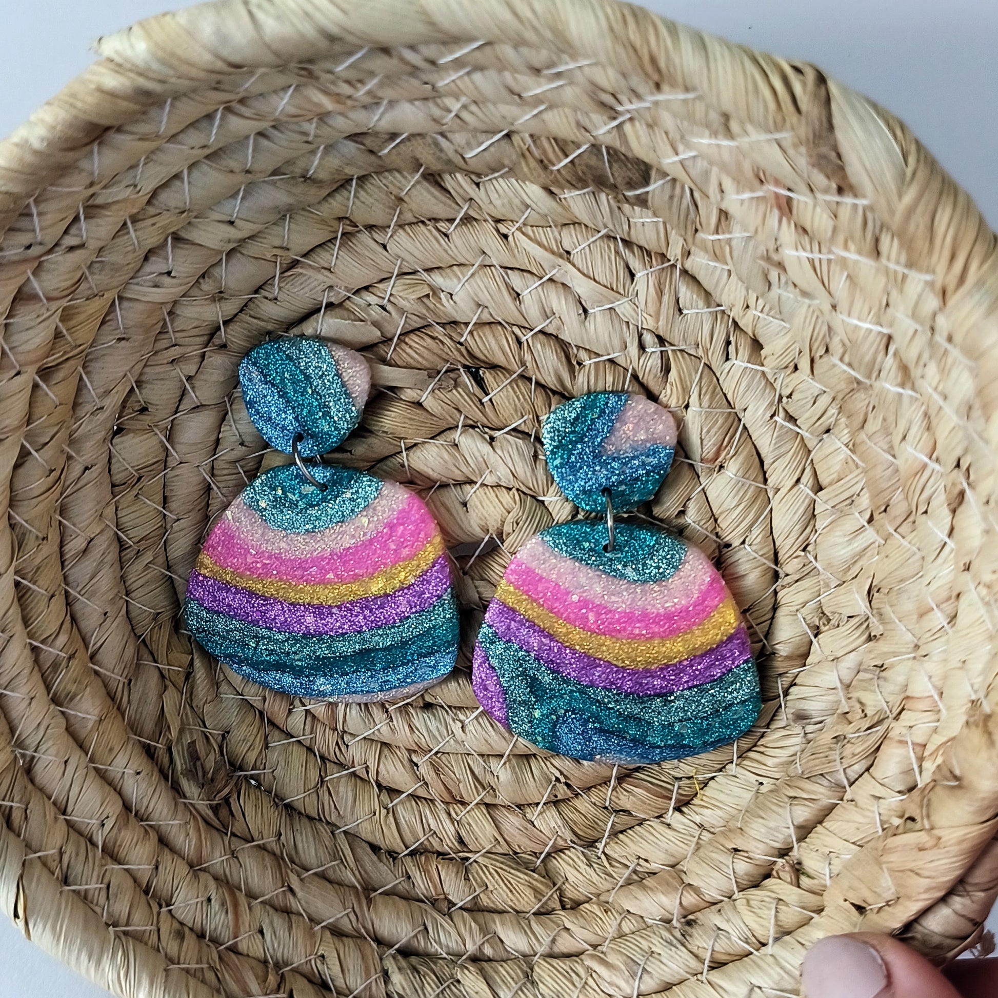 Colorful striped sparkle polymer clay earrings on a woven basket.