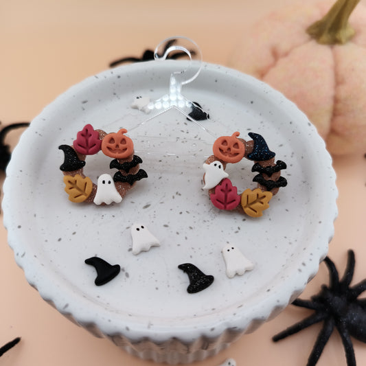 Halloween-themed earrings on a white dish with pumpkins and spider in the background