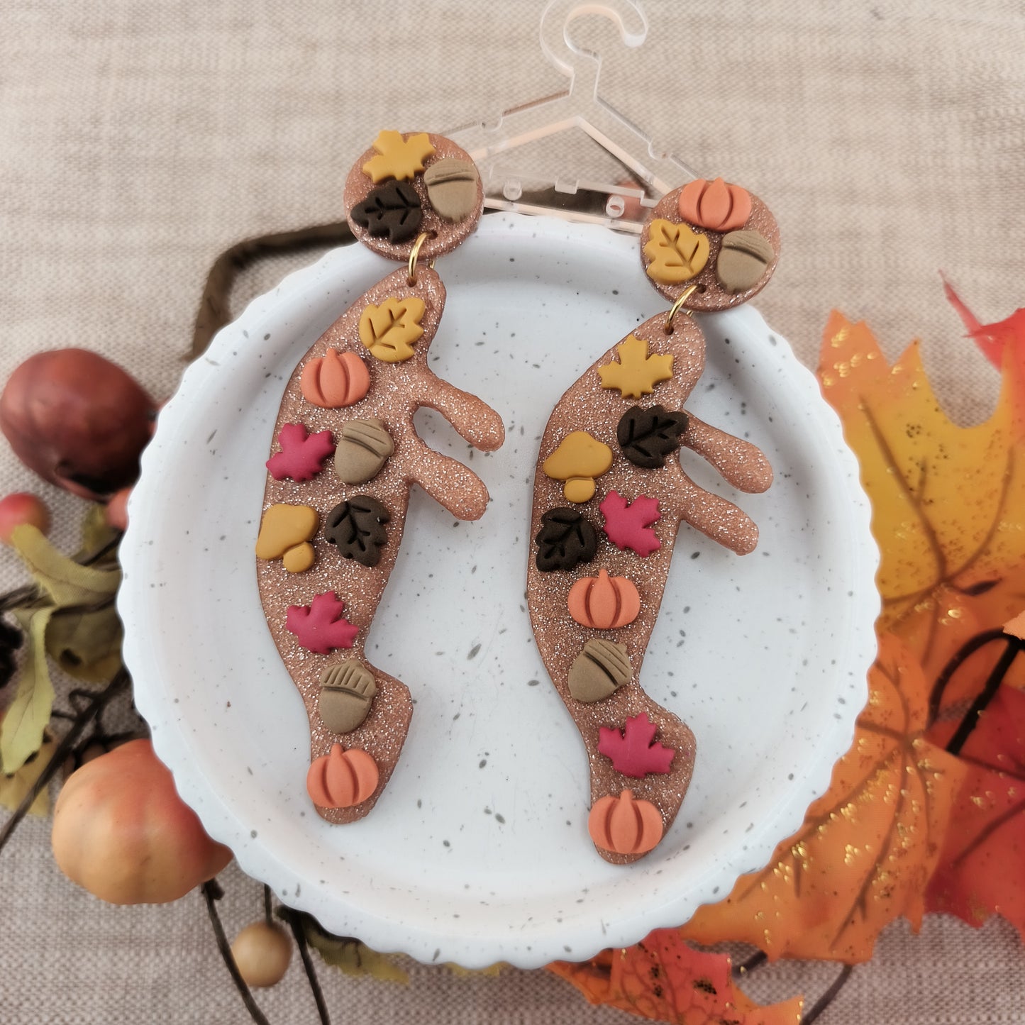 Pair of manatee earrings with autumn-themed design on a white plate with leaves and fruits in the background.