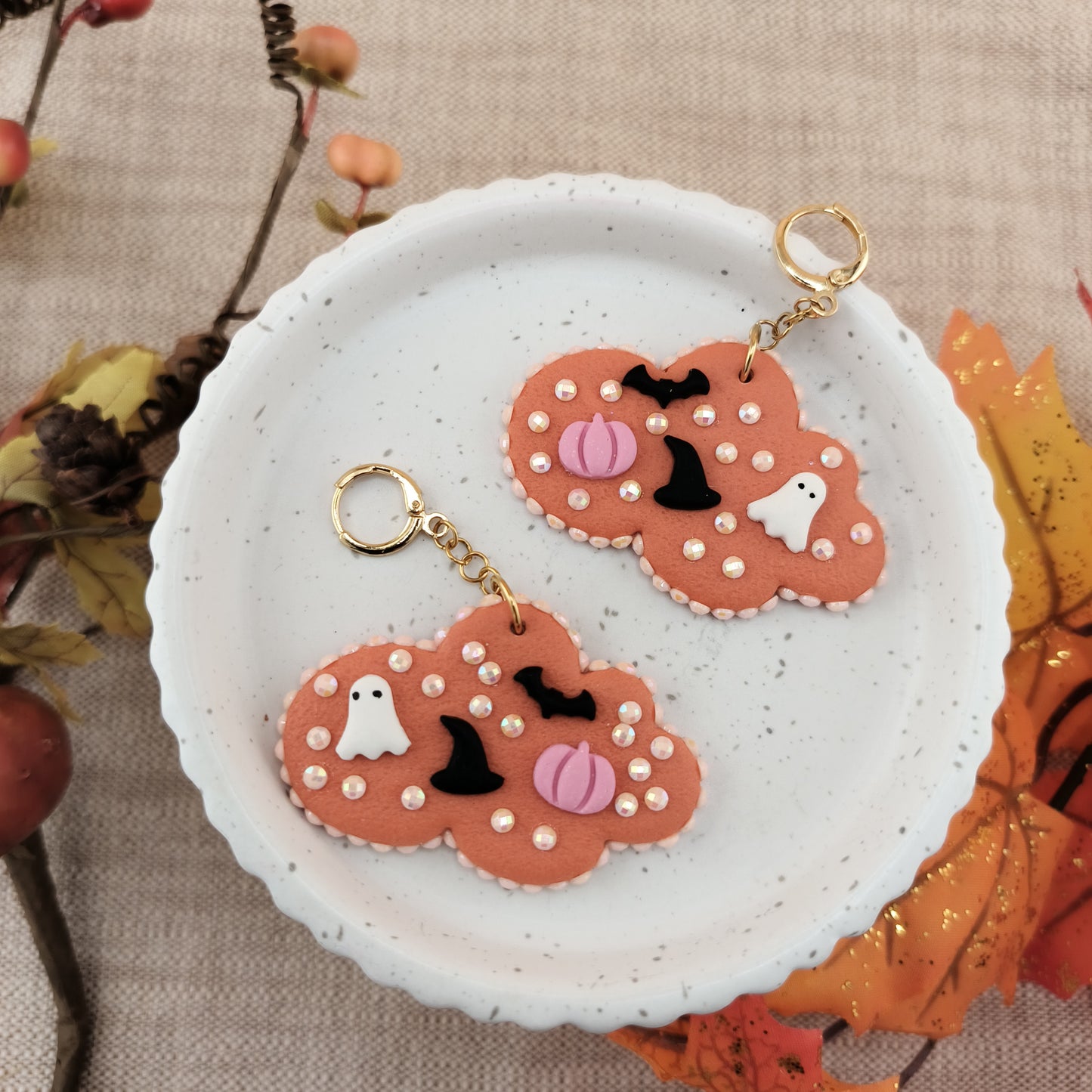 Two Halloween-themed earrings on a white plate with autumn leaves in the background.
