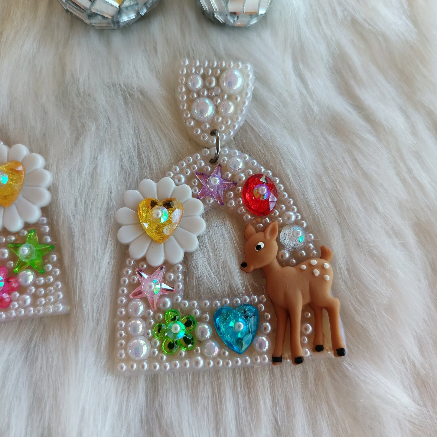 Bedazzled earrings with deer and floral designs on a fluffy white surface.