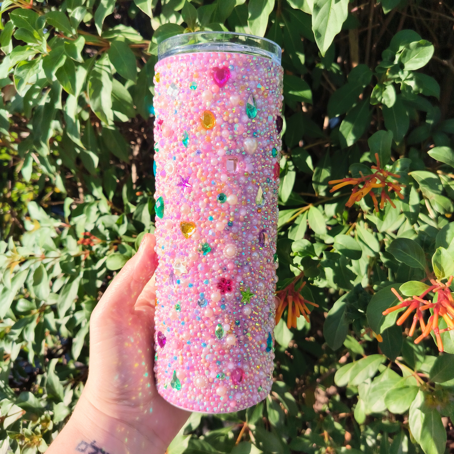 Colorful bedazzled tumbler held in front of green foliage