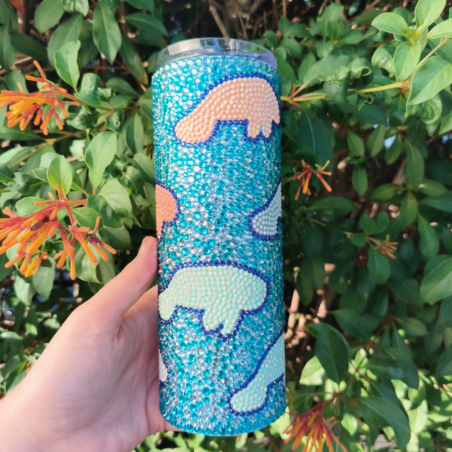 Tumbler with manatee design held in front of green foliage