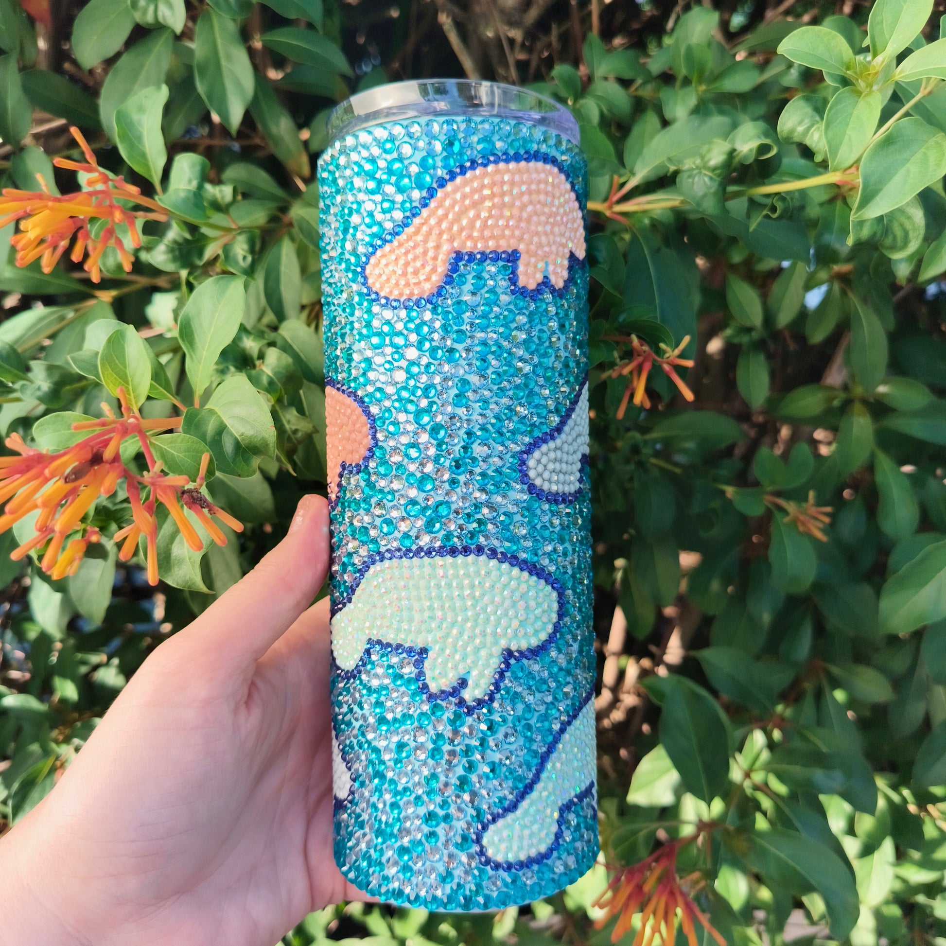 Tumbler with manatee design held in front of green foliage