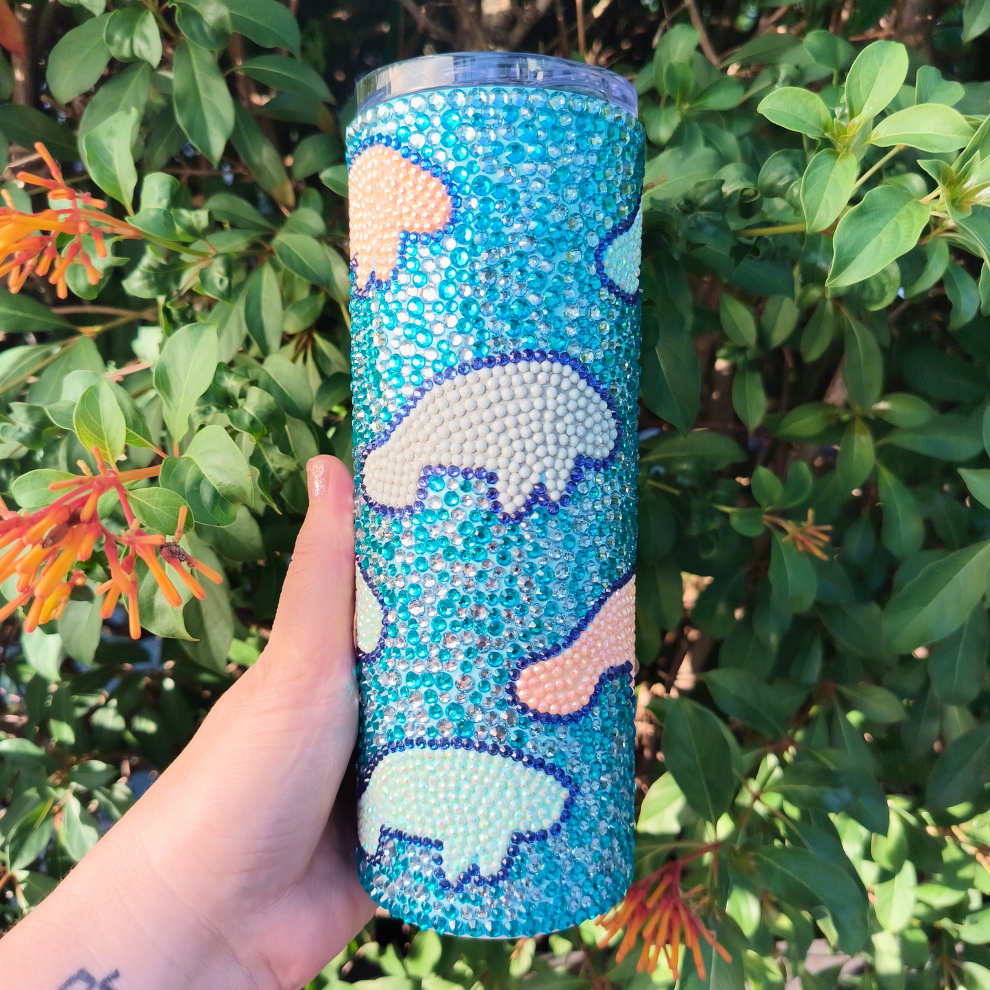 Blue tumbler with manatee design held in front of green foliage