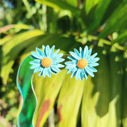 Blue daisy earrings on a green leafy background