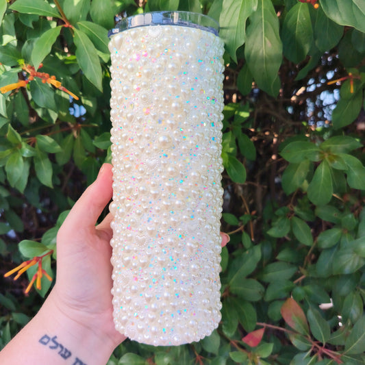 Hand holding a white bedazzled tumbler in front of green foliage