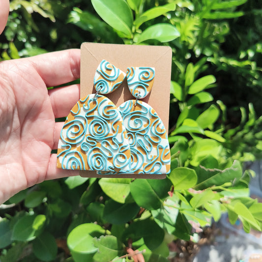 Large, dangle earrings that are white and mustard checkerboard , with a swirly blue design on top