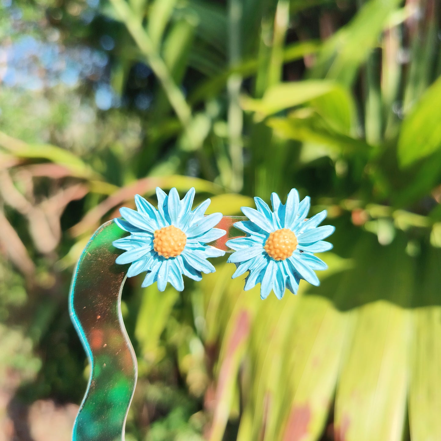 Blue daisy polymer clay stud earrings against a background of plants