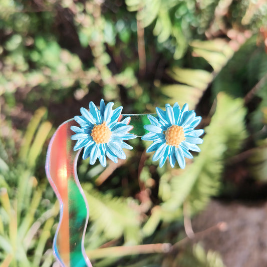 Blue flower earrings against a green leafy background