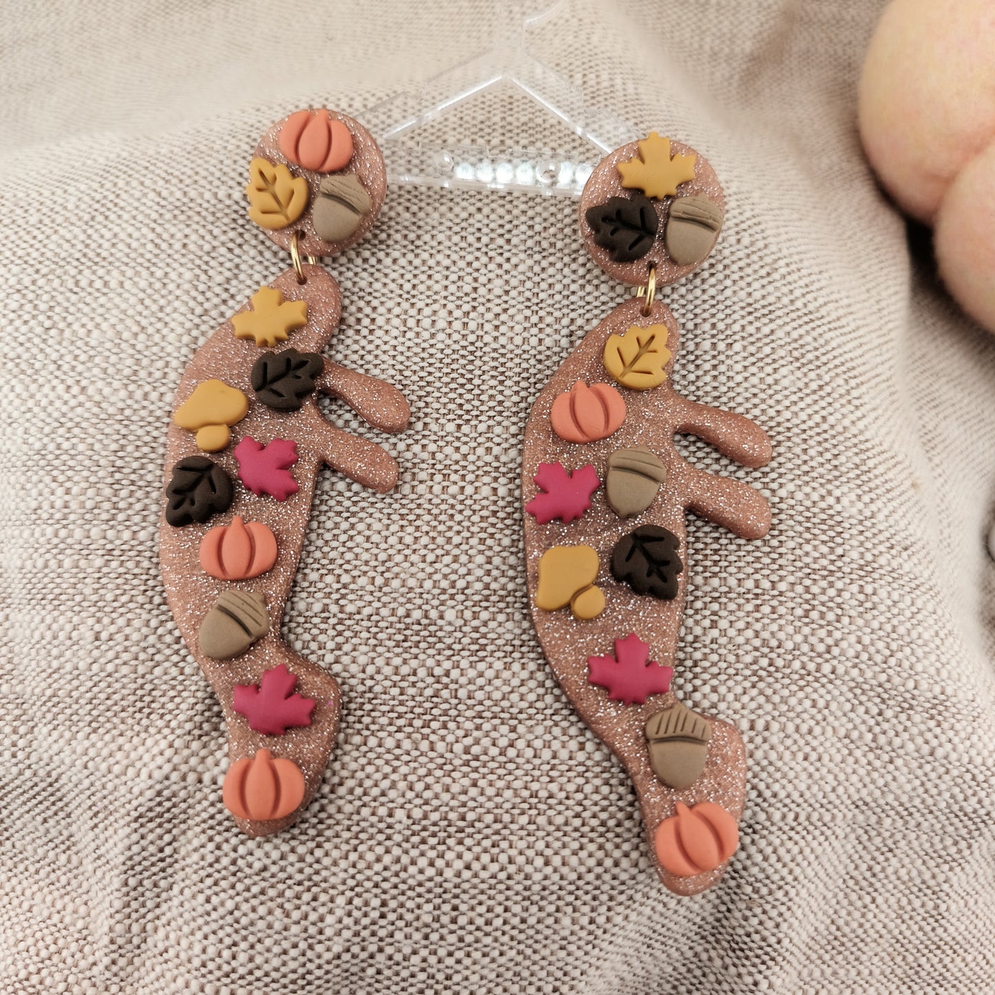 Pair of manatee earrings with colorful leaf and pumpkin designs on a textured surface.