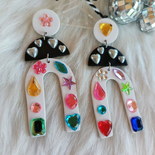 Colorful earrings with heart and star designs on a fluffy white surface.