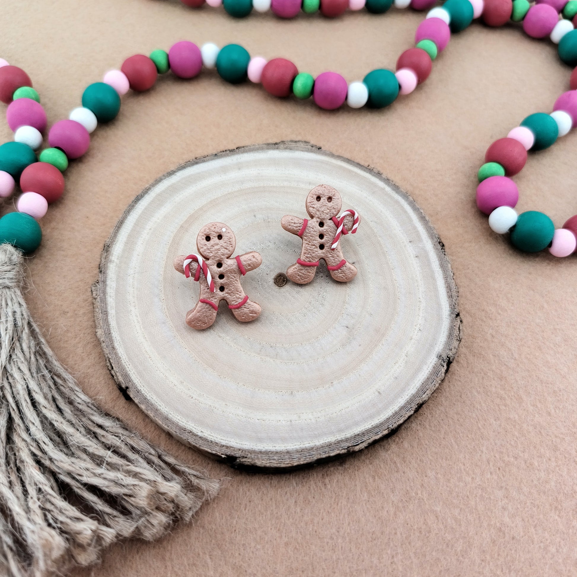 Two gingerbread man earrings on a wooden disc with a colorful bead garland in the background.