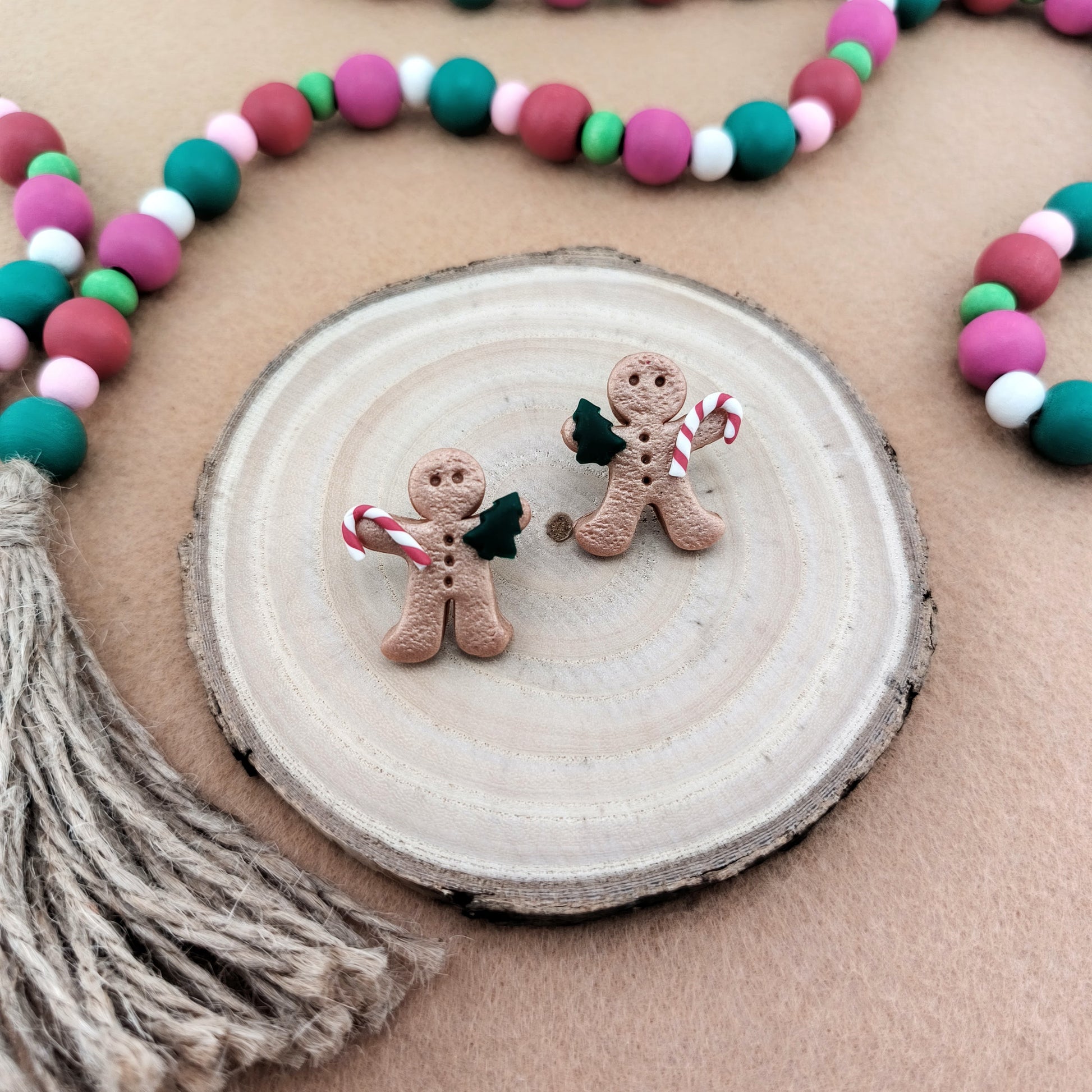 Two gingerbread man earrings on a wooden disc with colorful garland and tassel.
