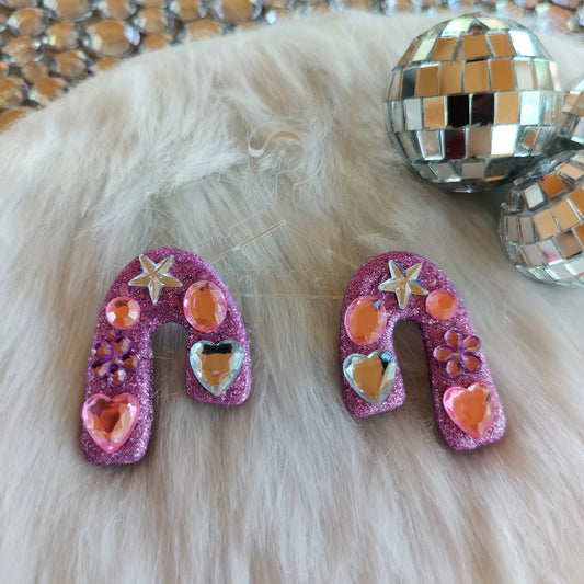 Pair of pink glittery earrings with heart and star designs on a fluffy white surface.